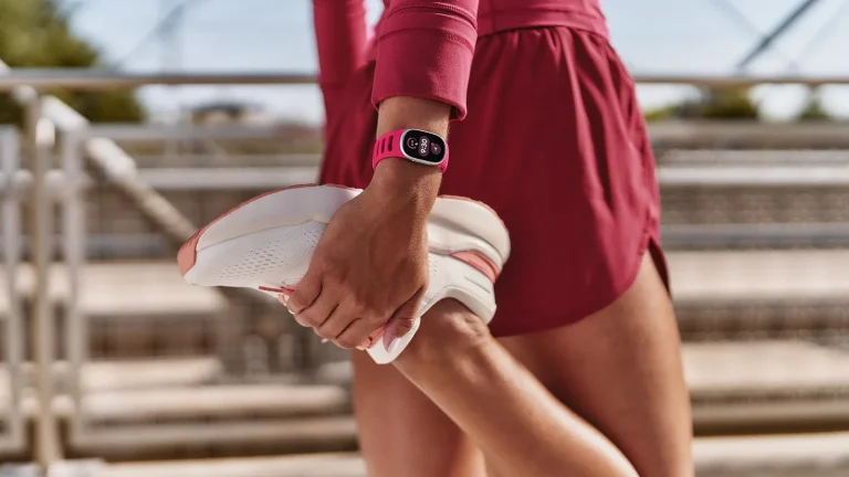 Le Fitbit Edge avec un bracelet Active Sport rose, porté au poignet par une coureuse qui s’étire