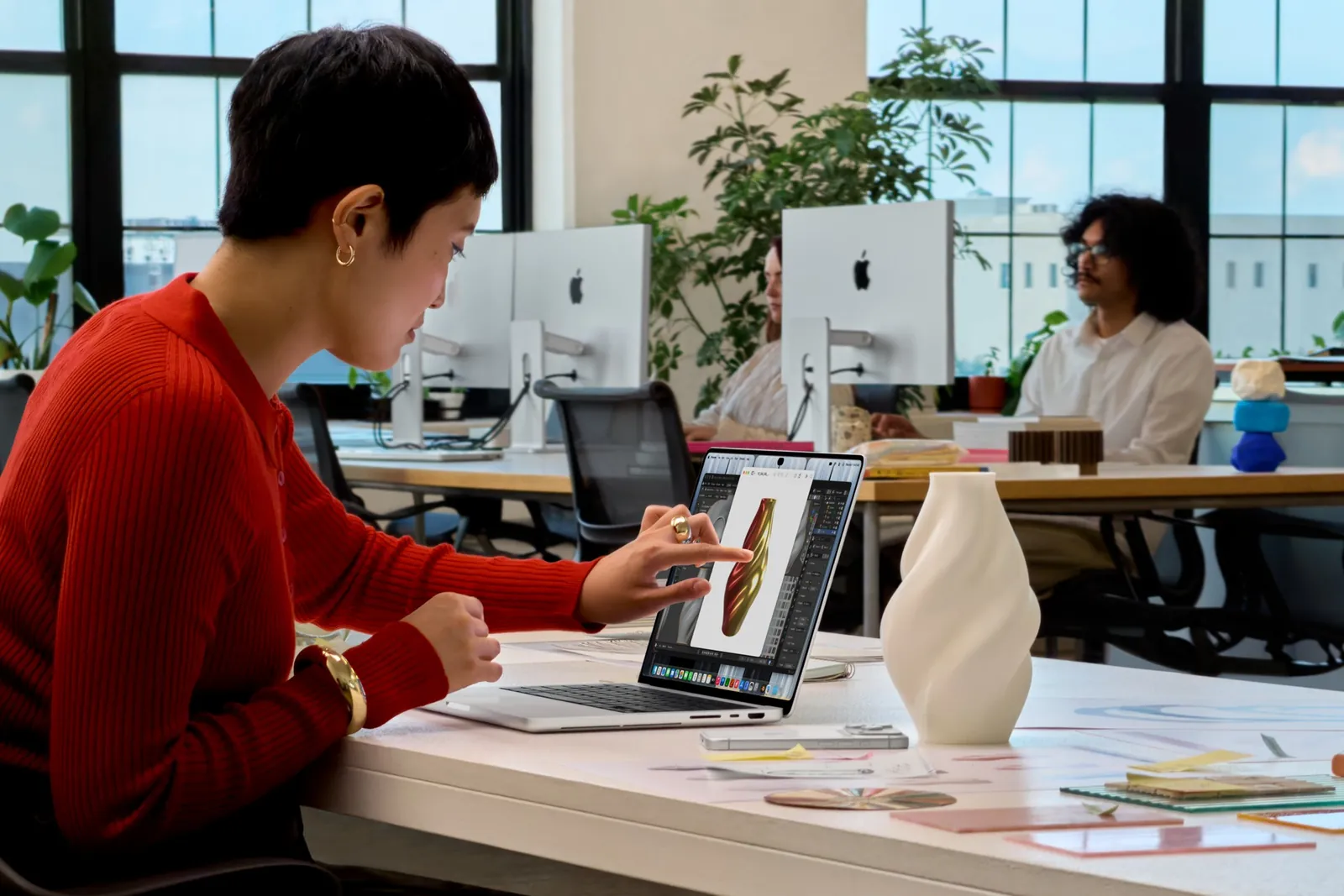 Une personne touche l’écran d’un MacBook Pro avec Écran PROLED XDR posé sur un bureau